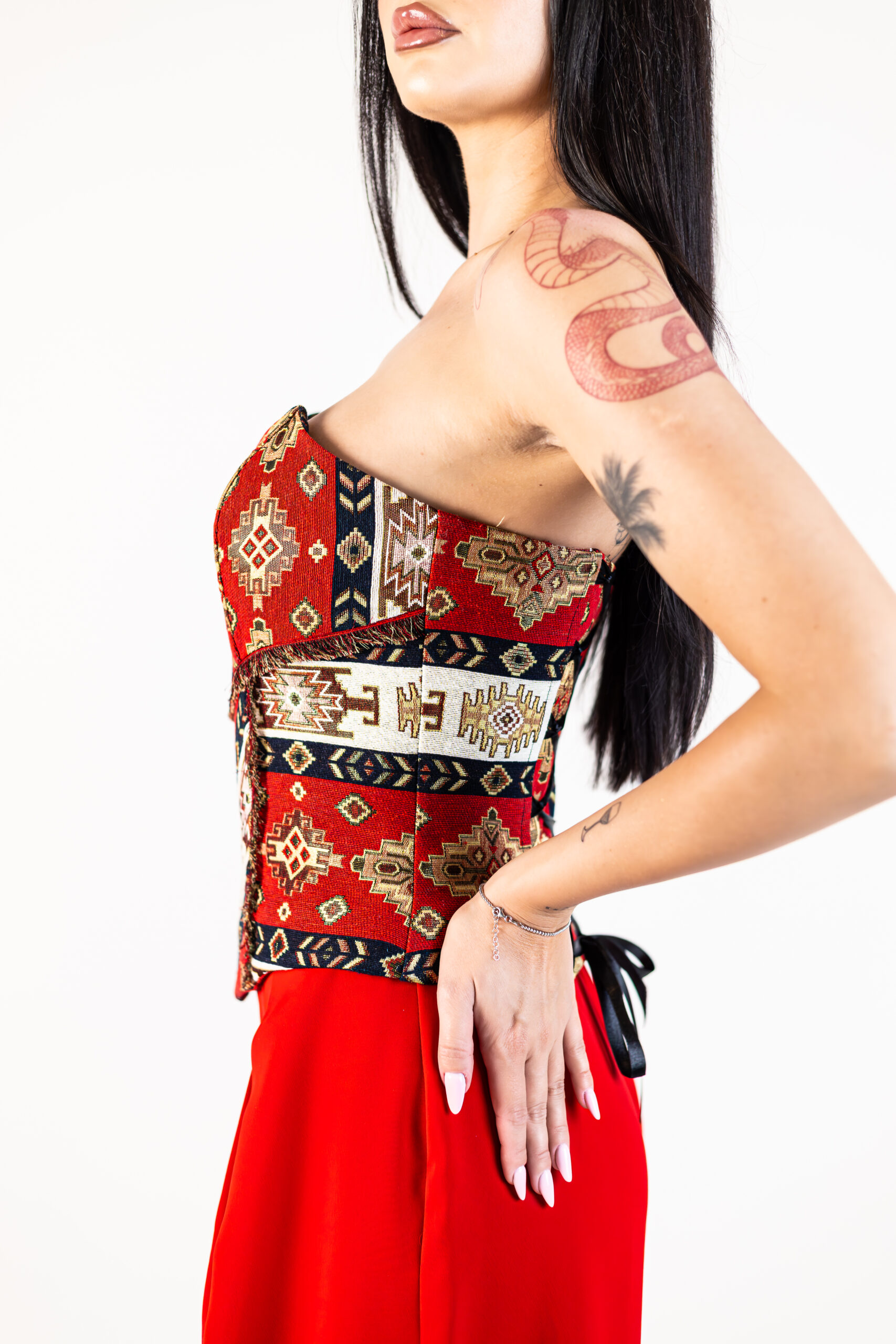 Corset Tessina Roșu din brocart fără bretele, cu motive geometrice și șnur reglabil din satin la spate, purtat cu pantaloni roșii eleganți.