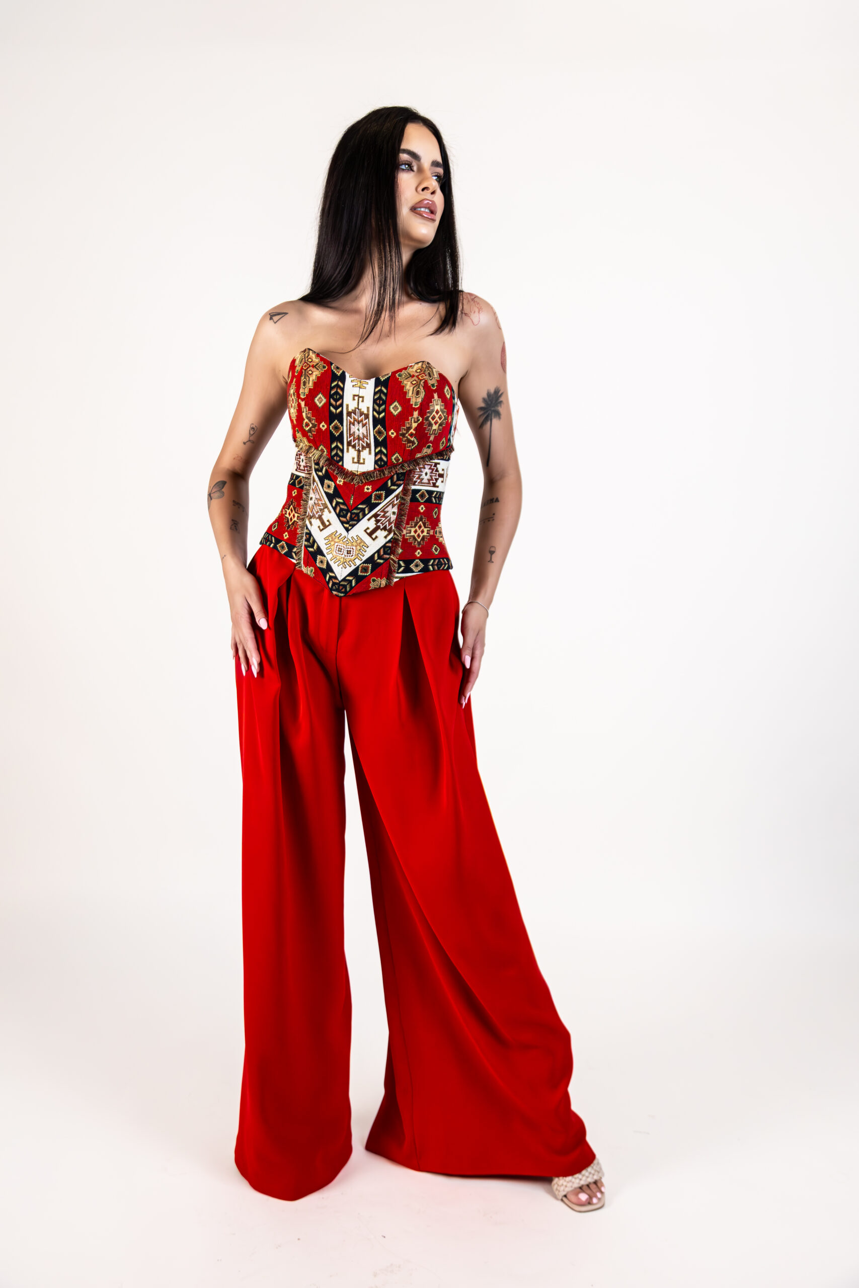Corset Tessina Roșu din brocart fără bretele, cu motive geometrice și șnur reglabil din satin la spate, purtat cu pantaloni roșii eleganți.